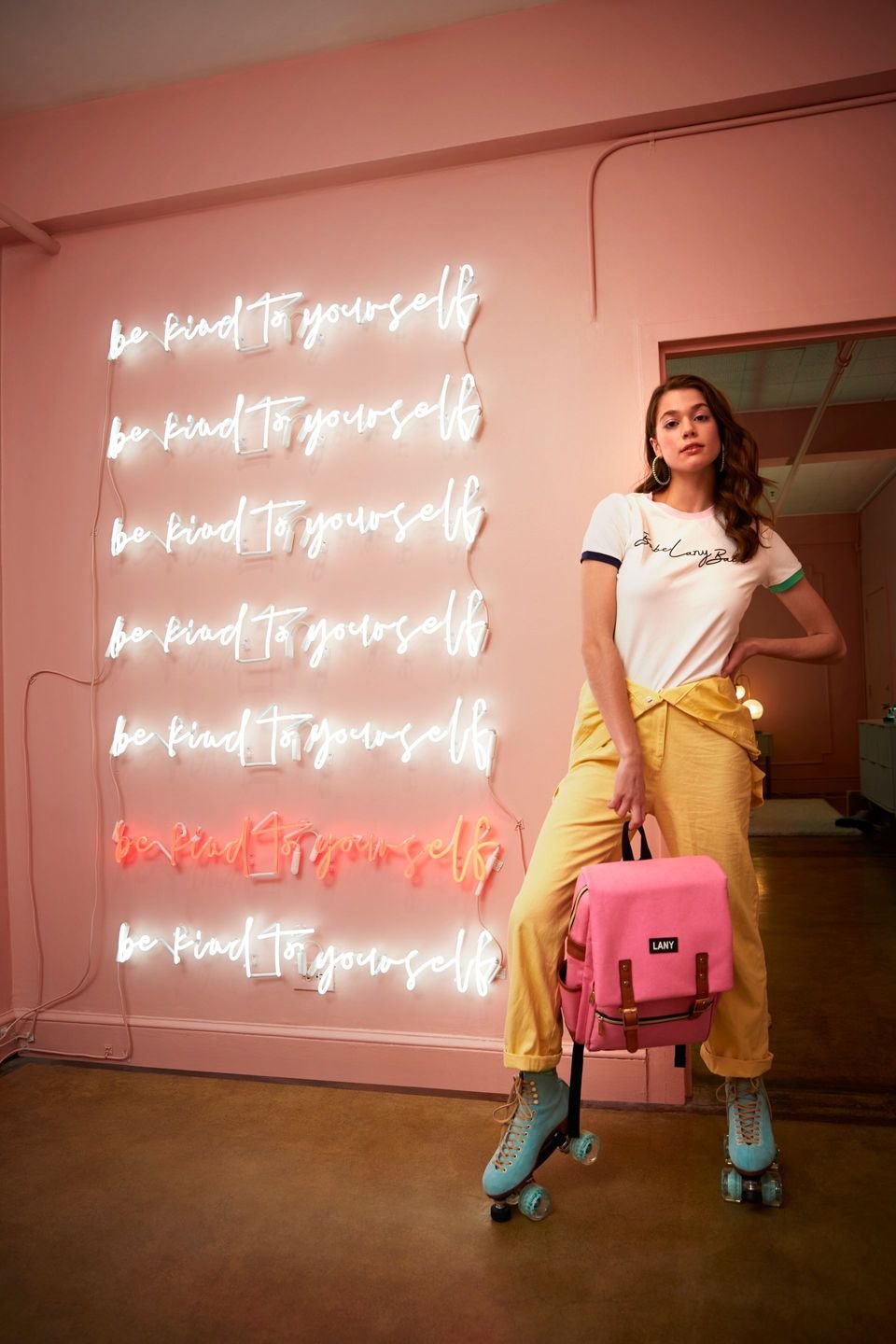 Woman in roller skates holding a pink backpack in front of a wall of pink neon signs