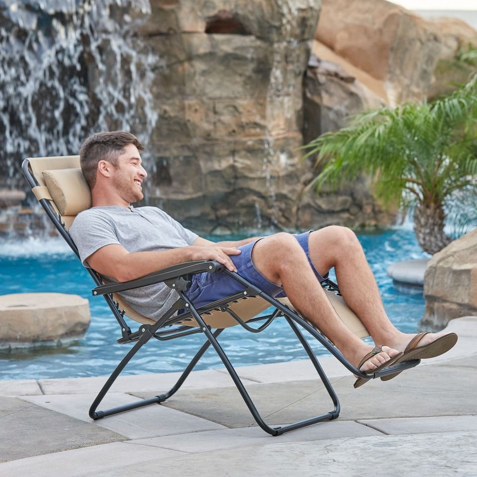 Man relaxing in a zero-gravity lounge chair beside a pool with a rock waterfall